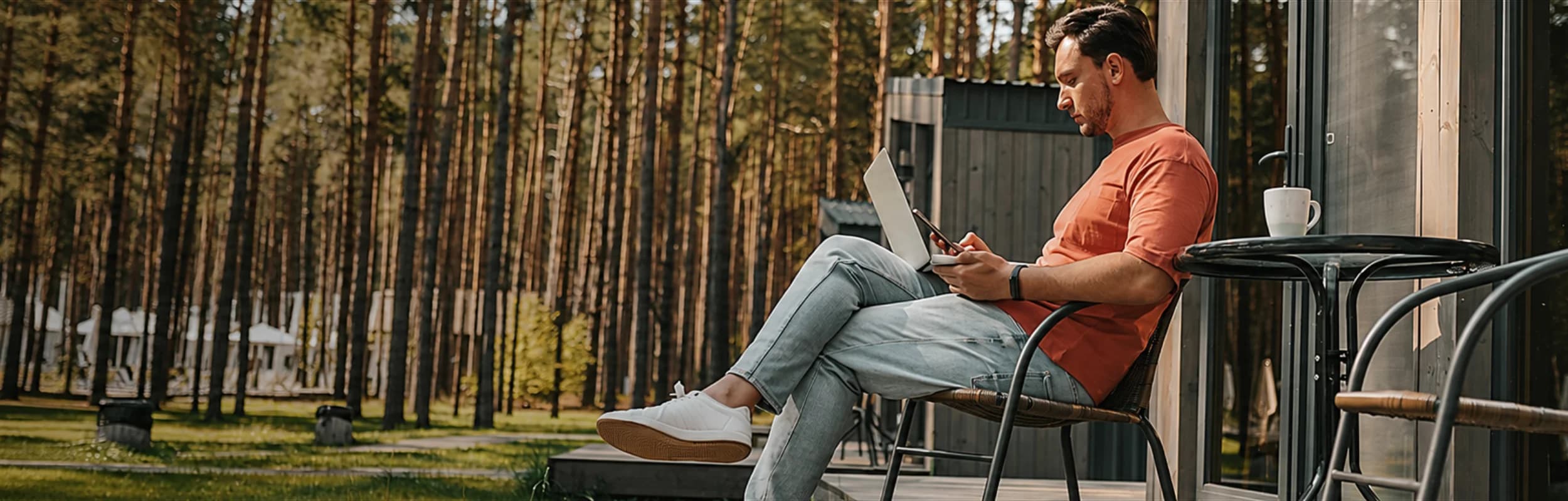 A man working on a laptop on the deck of a cabin in the woods